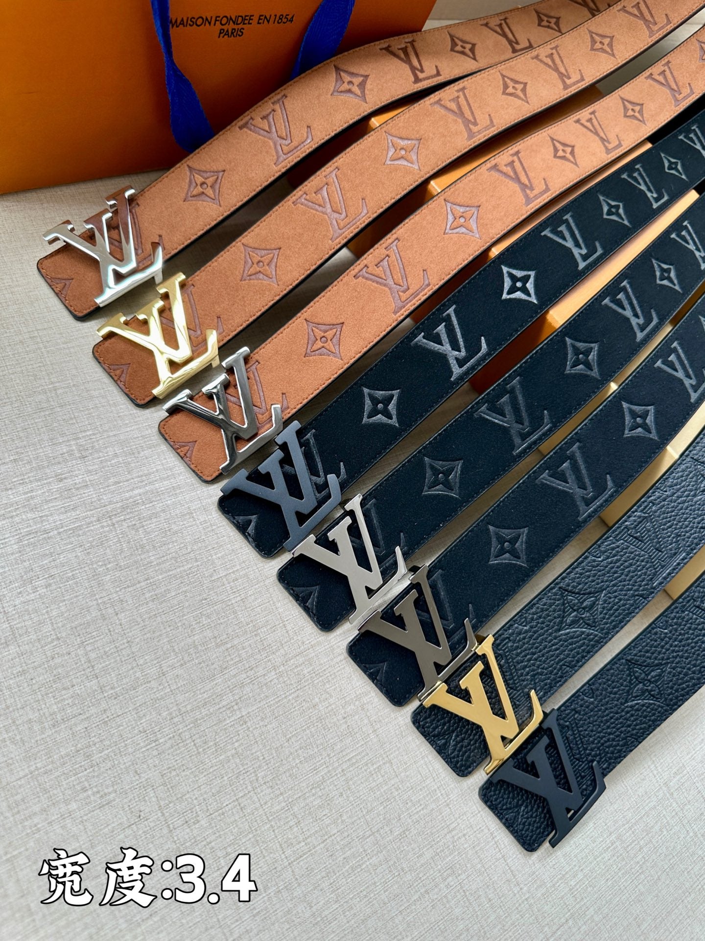 Monogram belts with tan and dark blue straps, each featuring an LV buckle