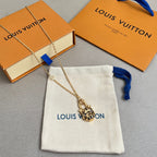 Gold-tone tiger-face pendant necklace with blue ribbon detail, on white Louis Vuitton pouch