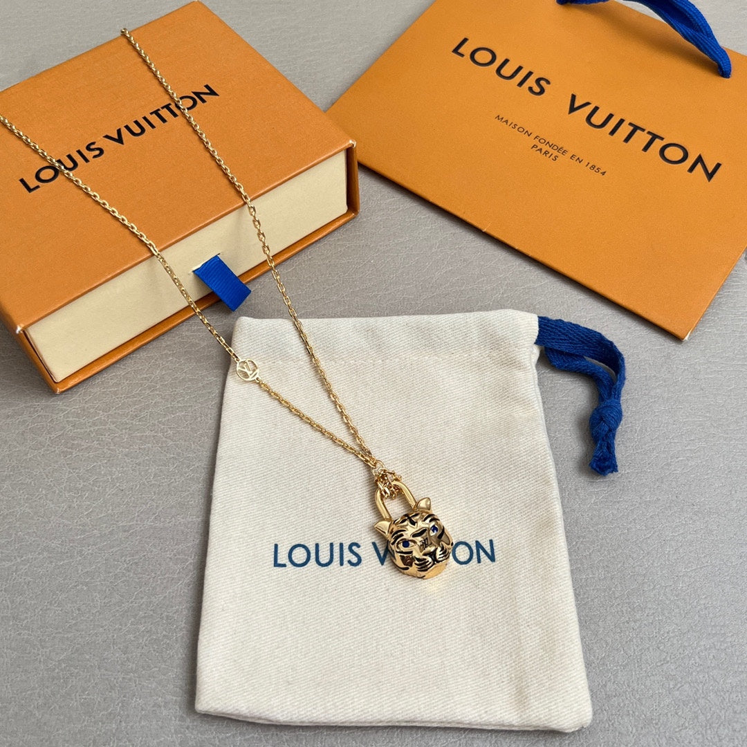 Gold-tone tiger-face pendant necklace with blue ribbon detail, on white Louis Vuitton pouch