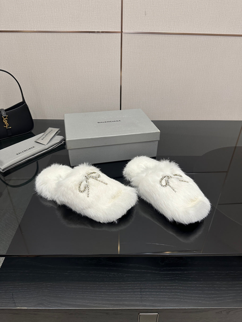 Pair of white faux fur slide sandals with silver logo charm on strap