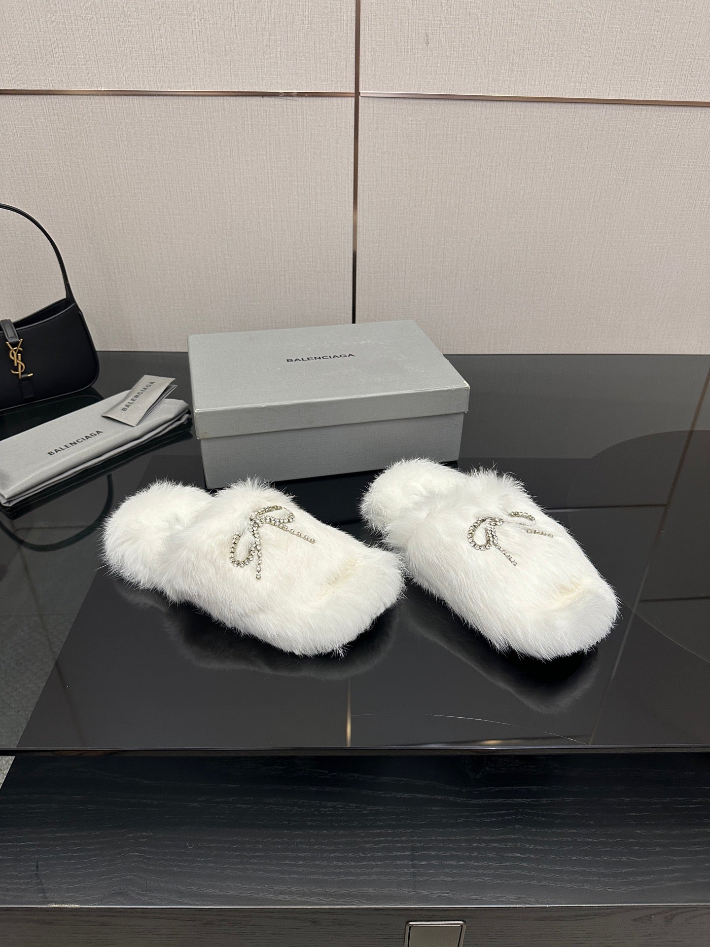 Pair of white faux fur slide sandals with silver logo charm on strap