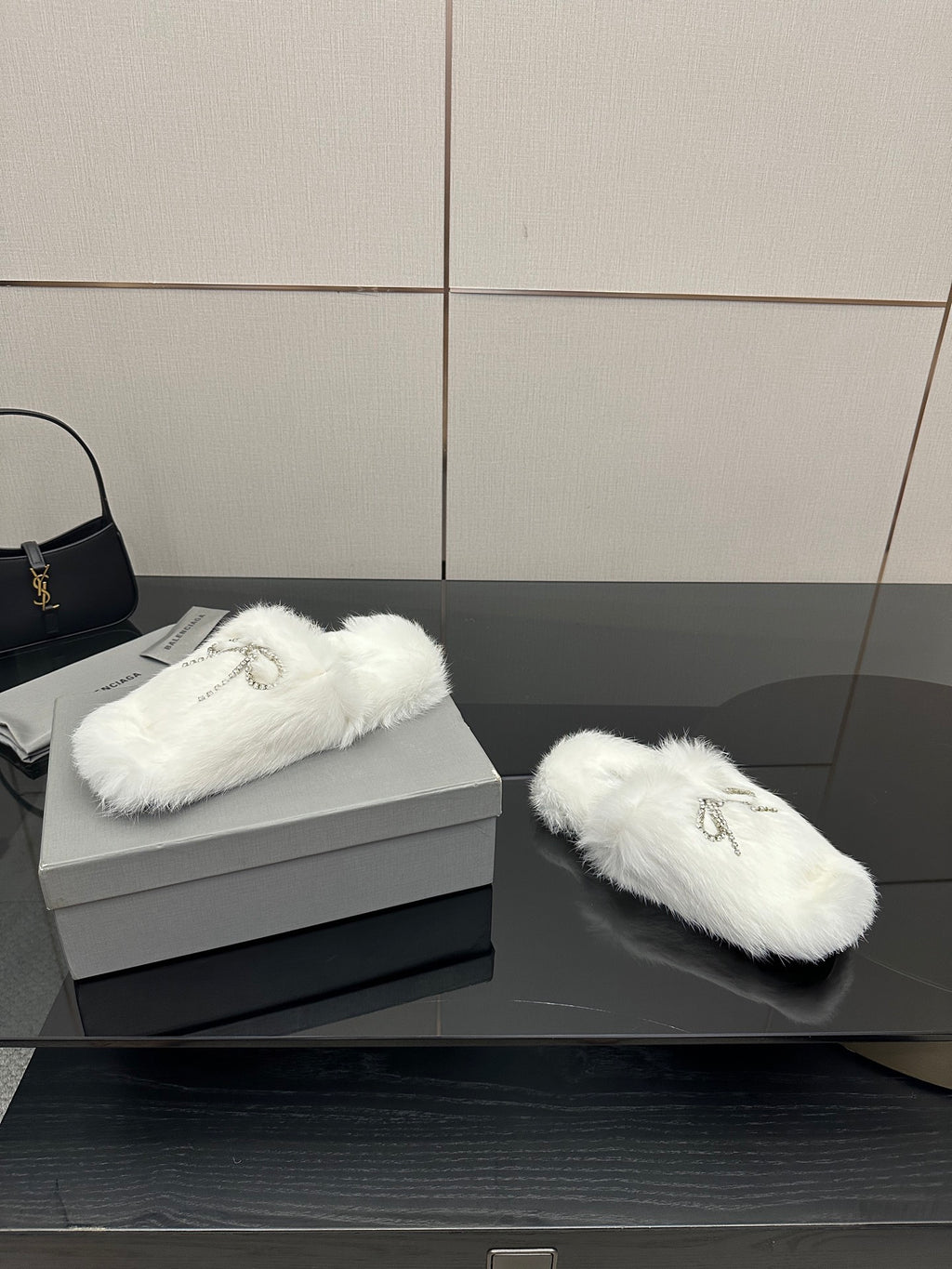 White faux fur slide sandals on display with silver logo charm on top