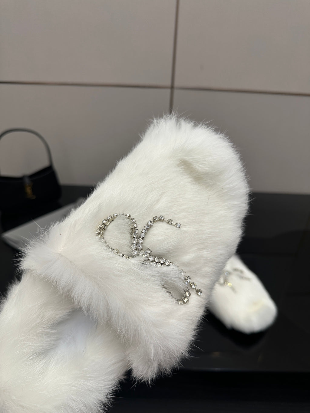 Close-up of white faux fur slide sandal with silver logo charm detail