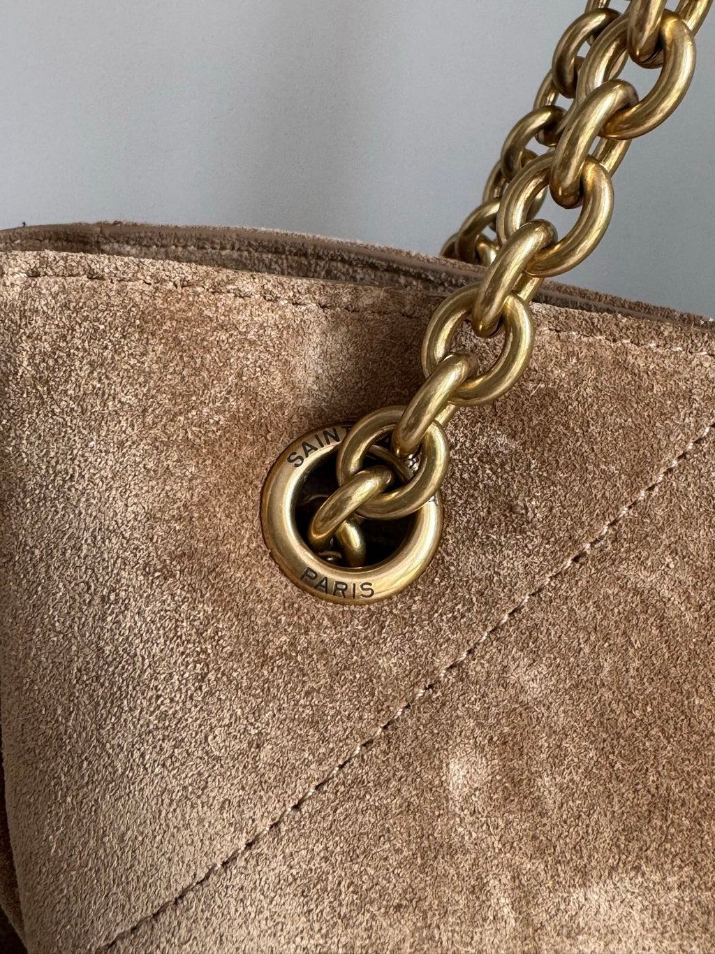 Gold chain attachment and round logo charm on tan suede bag