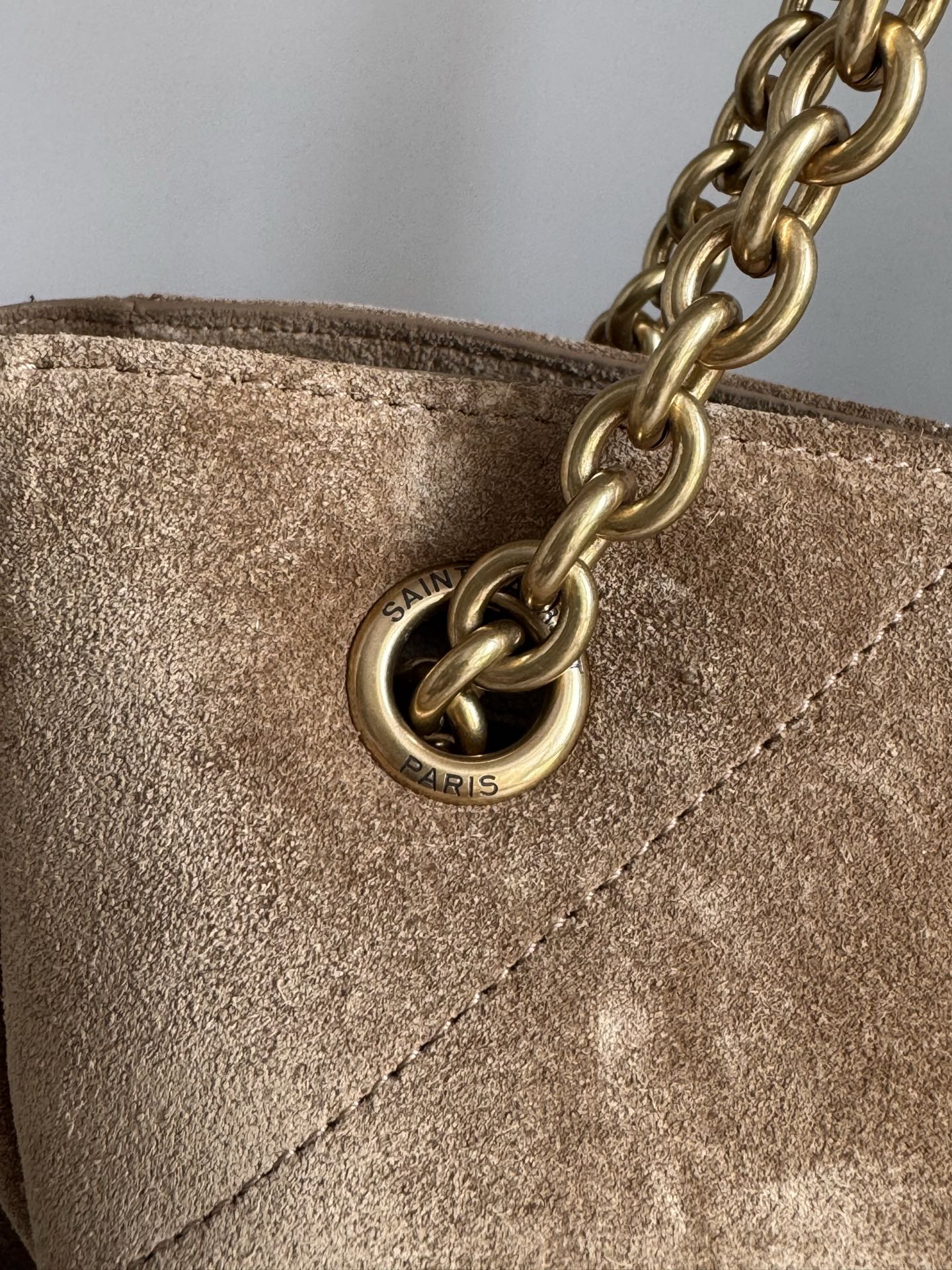 Gold chain attachment and round logo charm on tan suede bag