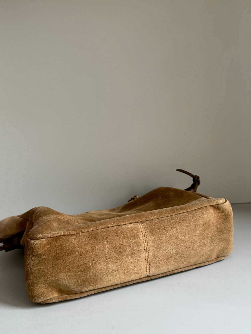 Tan suede tote bag laid on side with leather tie straps