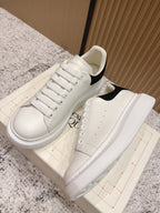White lace-up sneakers with black heel panel, side view, on shoebox