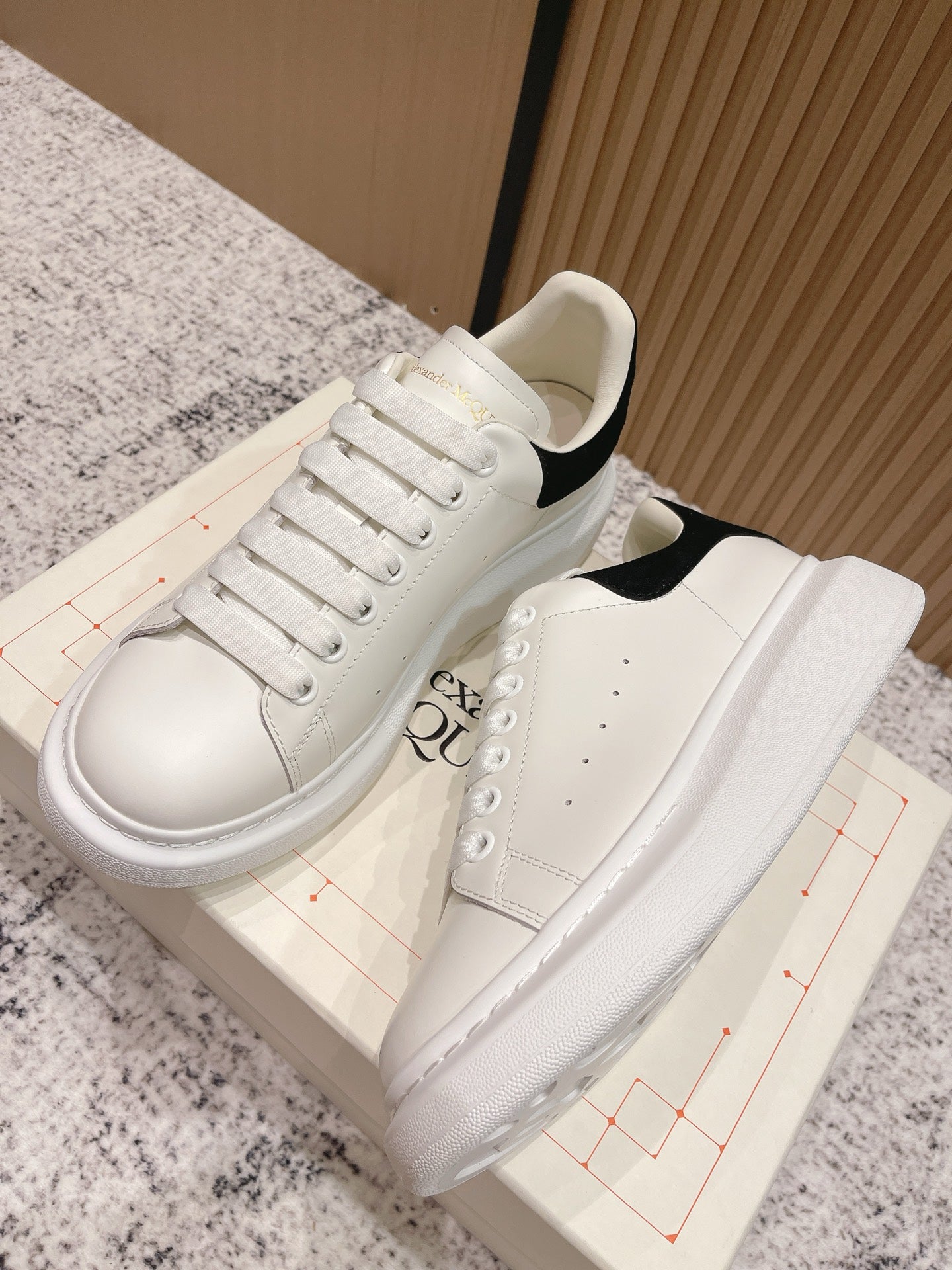 White lace-up sneakers with black heel panel, side view, on shoebox