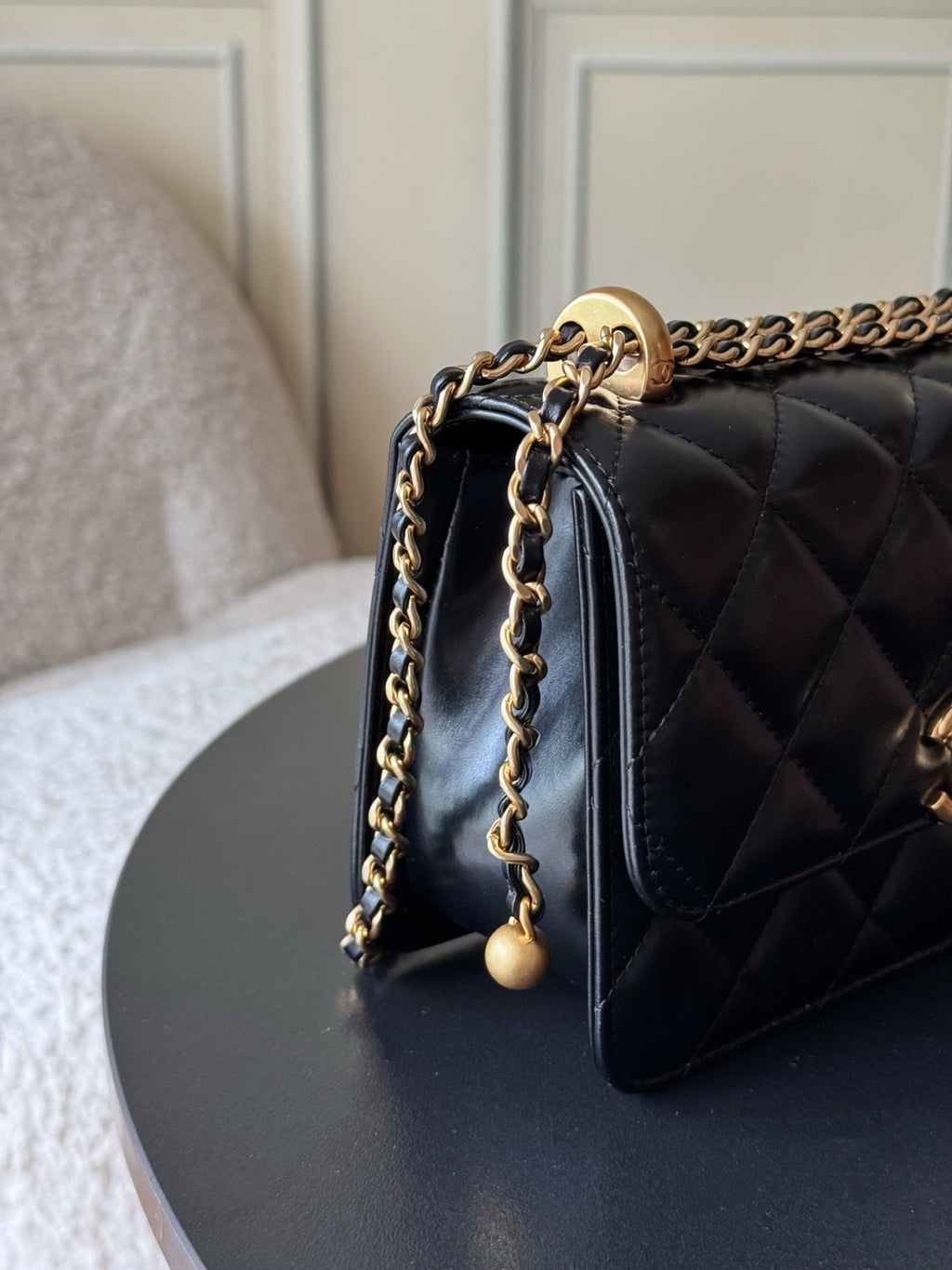 Side view of quilted black flap shoulder bag with gold chain and bead drops