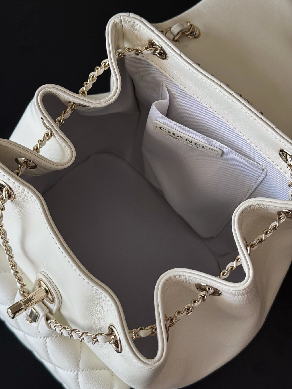 Chanel white quilted bucket bag interior with side opening and chain straps.