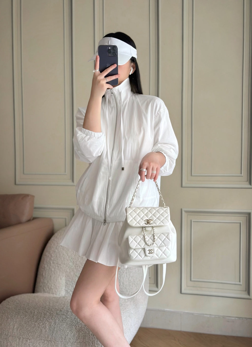 Chanel quilted white mini shoulder bag with chain strap held at waist.