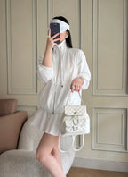 Chanel quilted white mini shoulder bag with chain strap held at waist.