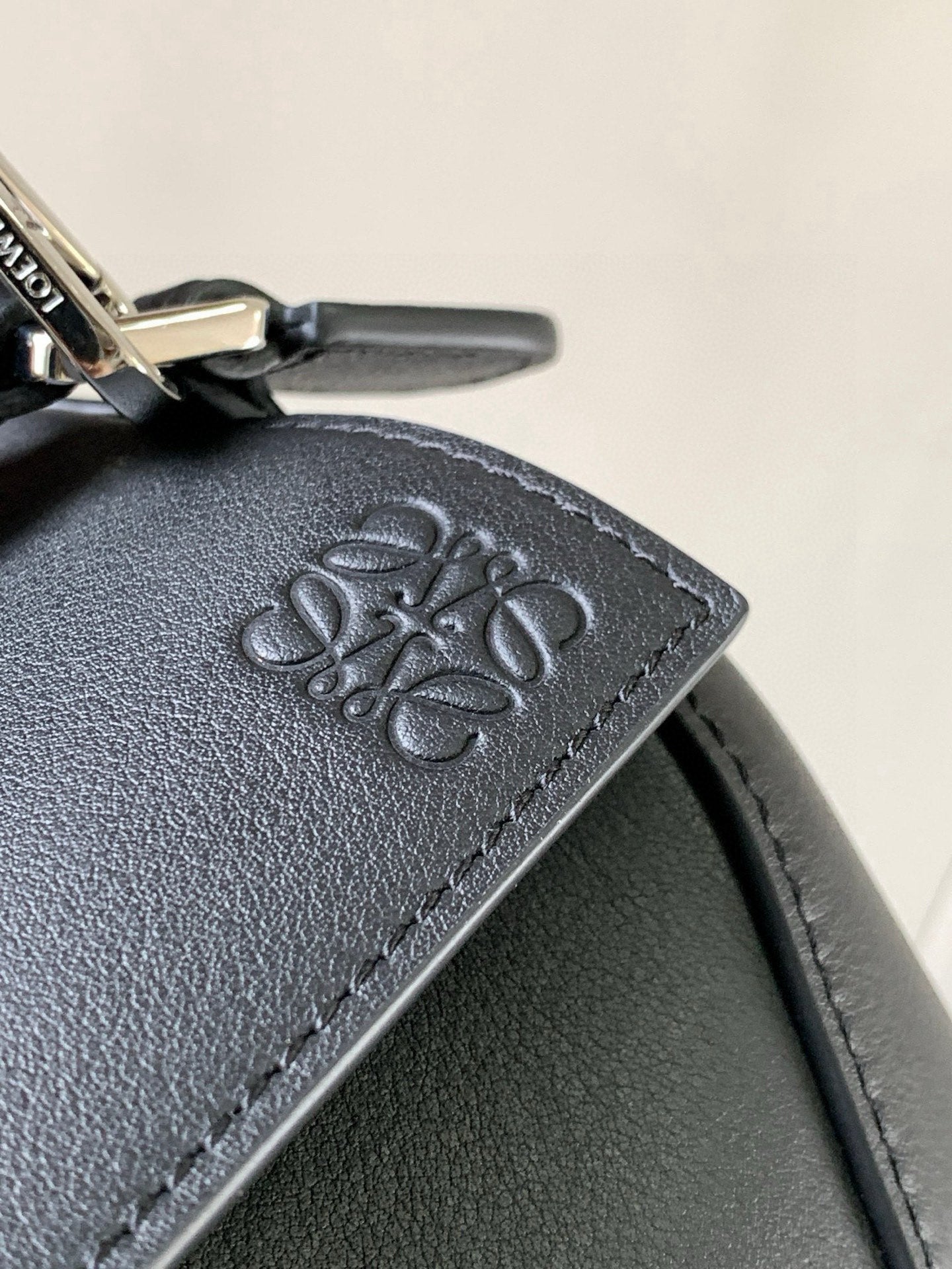 Embossed logo on dark leather bag corner with visible stitch edging