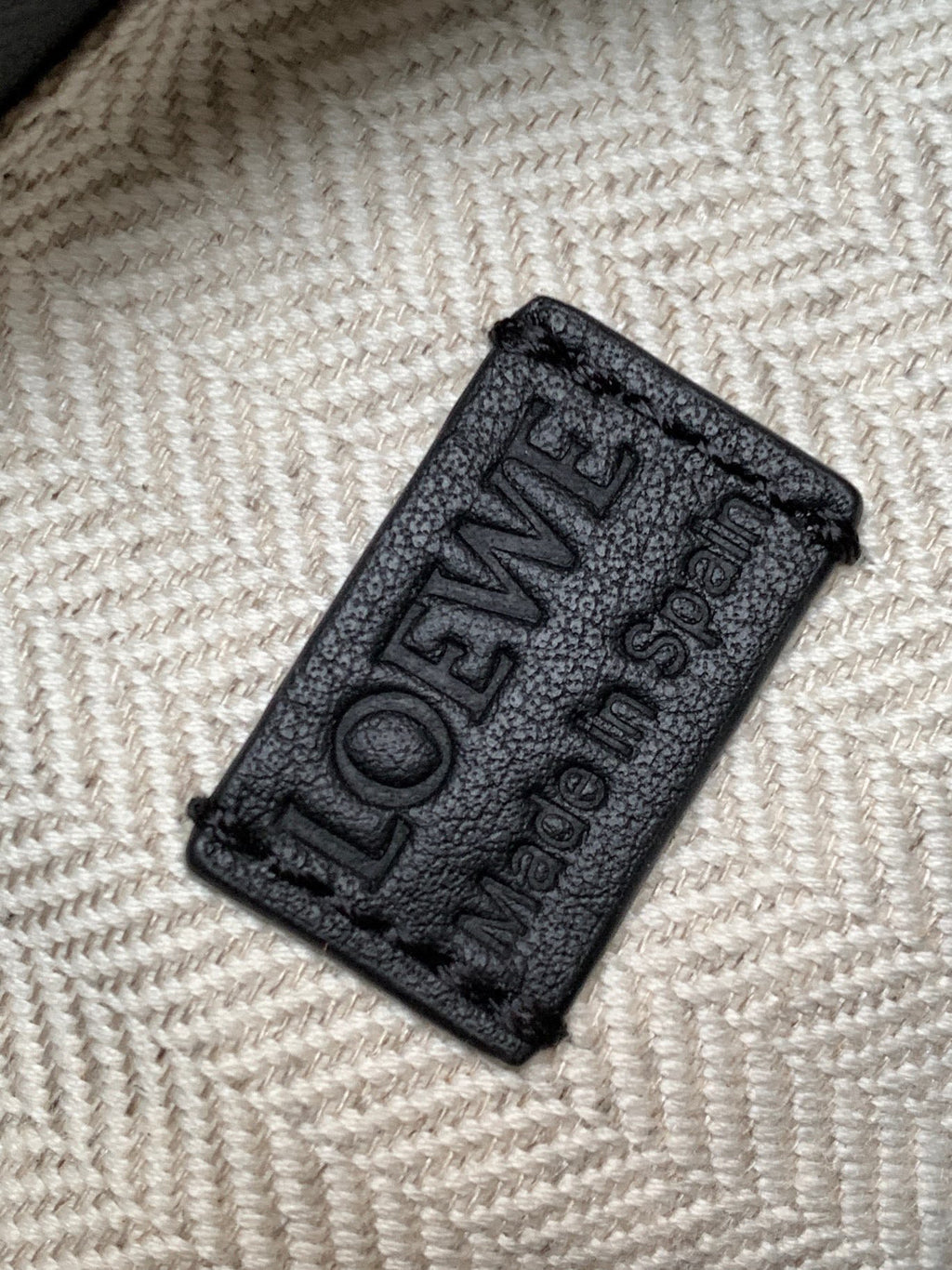 Black leather brand tag with embossed LOEWE lettering on textured background