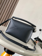 Dark leather top-handle bag with structured shape and crossbody strap, silver clasp