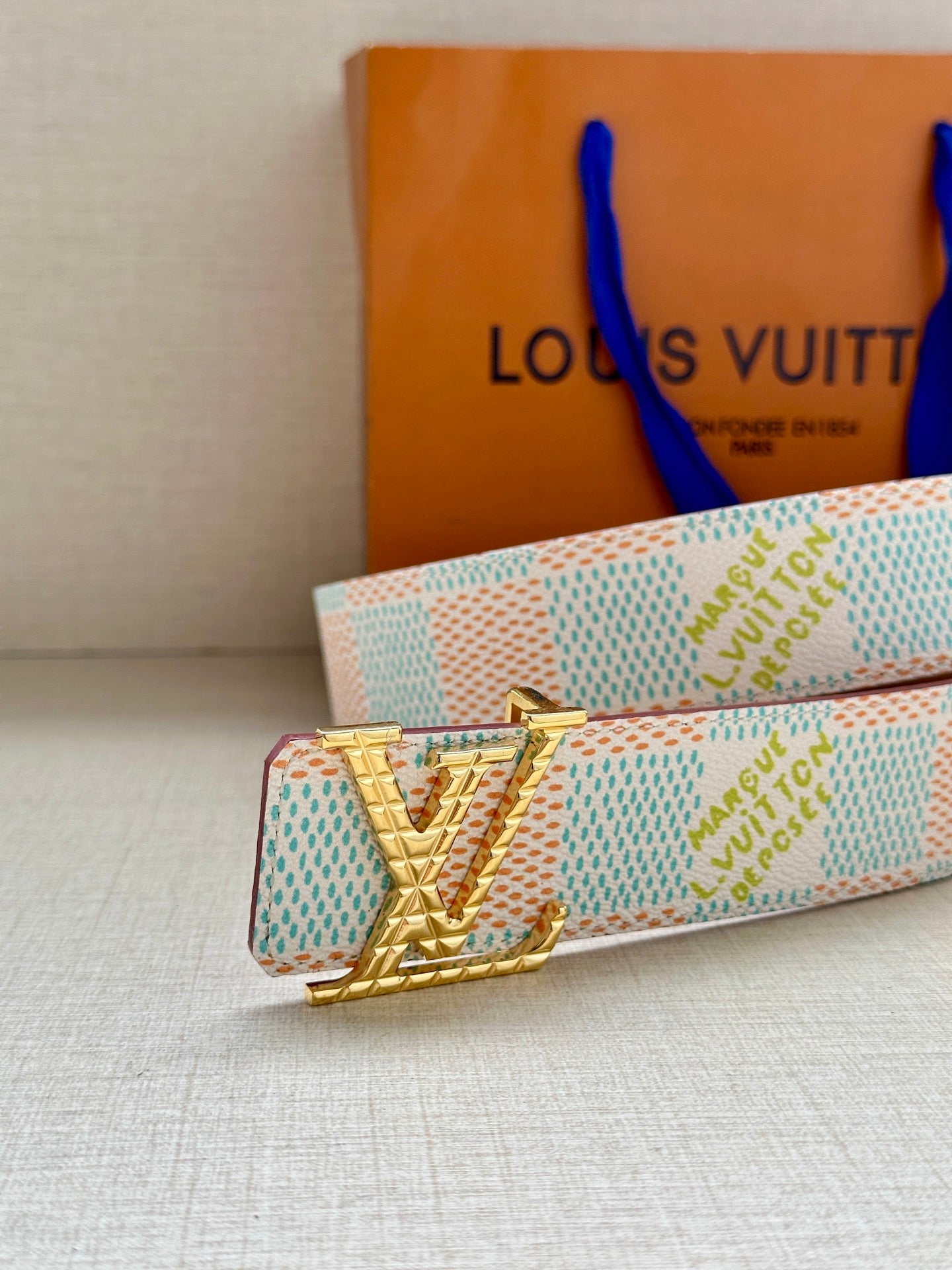 Louis Vuitton belt laid flat with gold V buckle on turquoise-and-white patterned strap