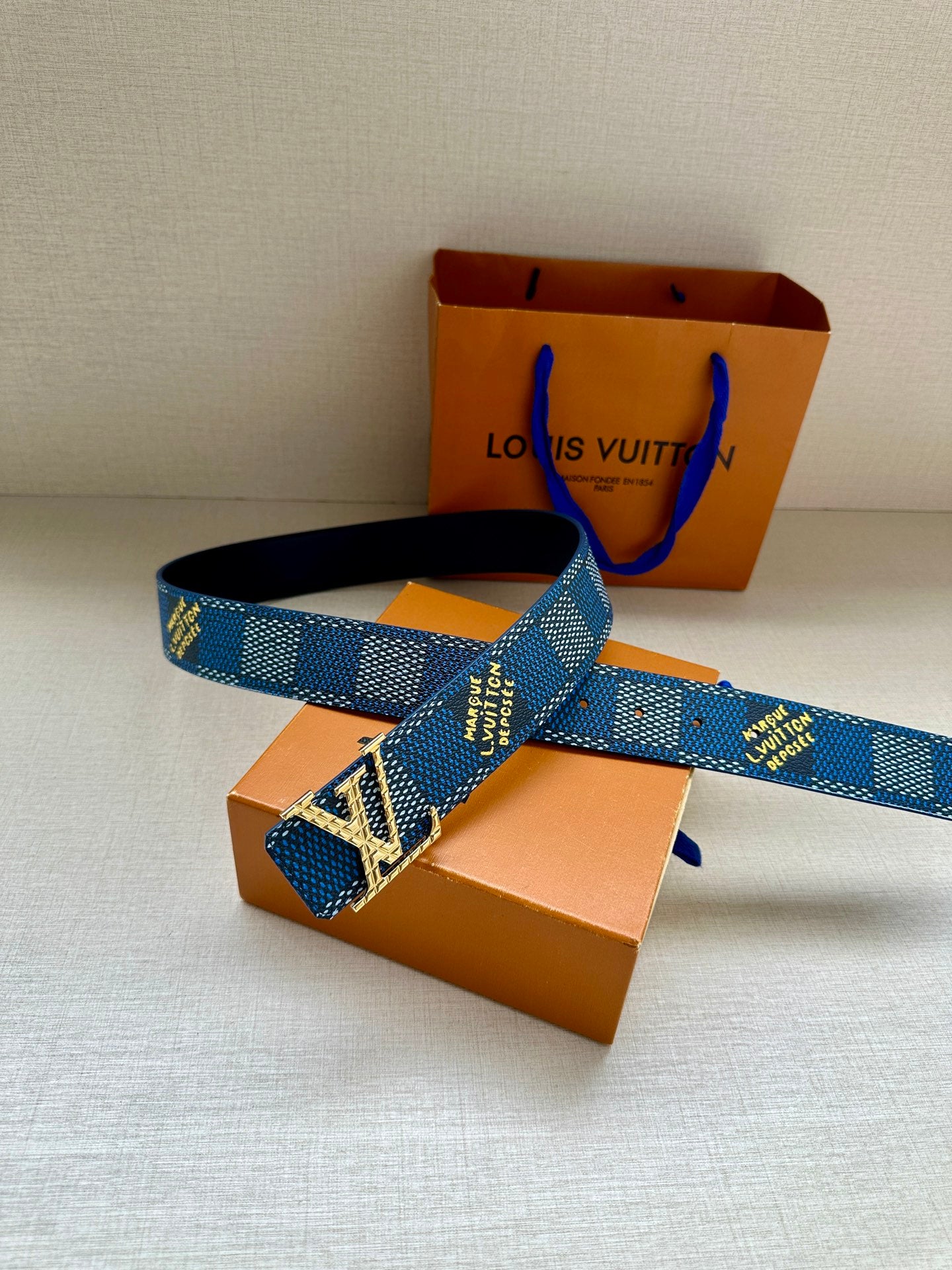 Blue patterned Louis Vuitton belt with large silver LV buckle, shown laid across