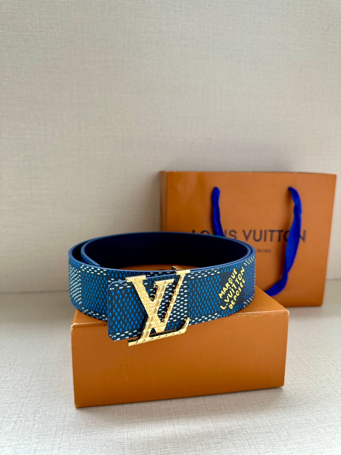 Blue patterned Louis Vuitton belt with silver LV buckle on a stack