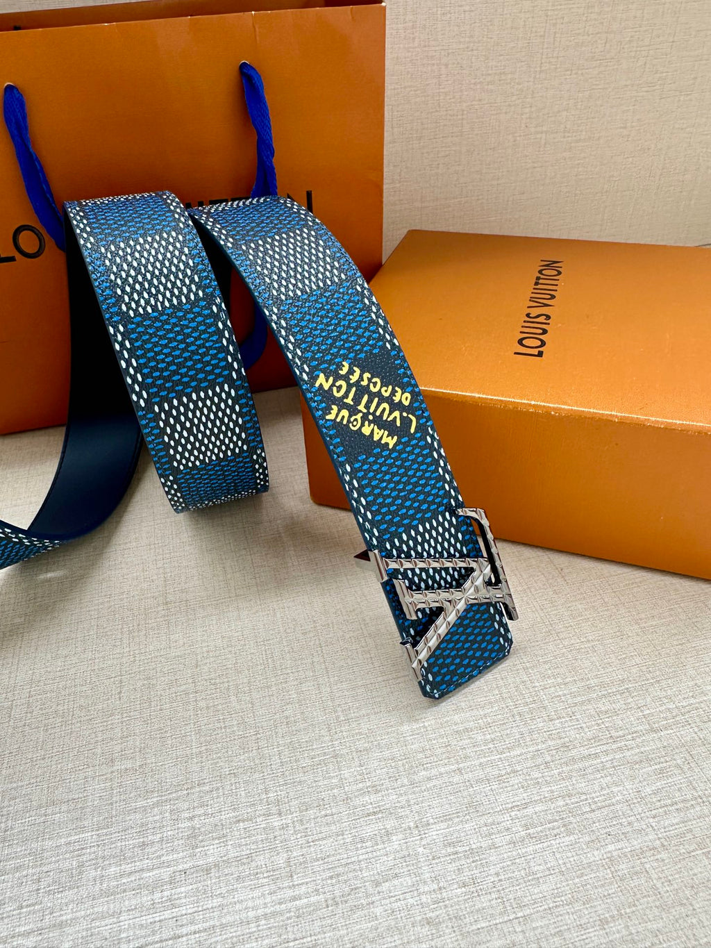 Blue patterned Louis Vuitton belt with square silver buckle, strap ends folded