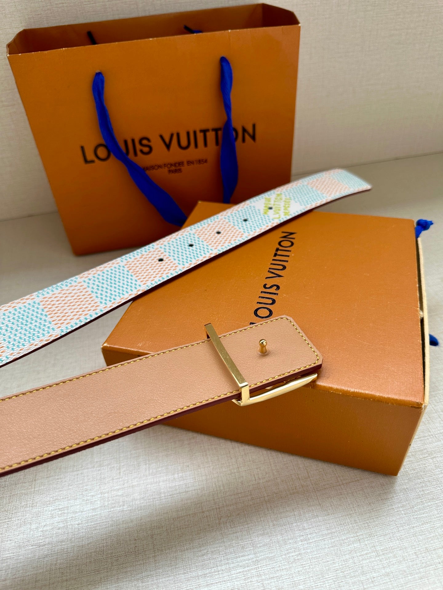 Louis Vuitton belt with light blue and white patterned strap and tan leather hardware.