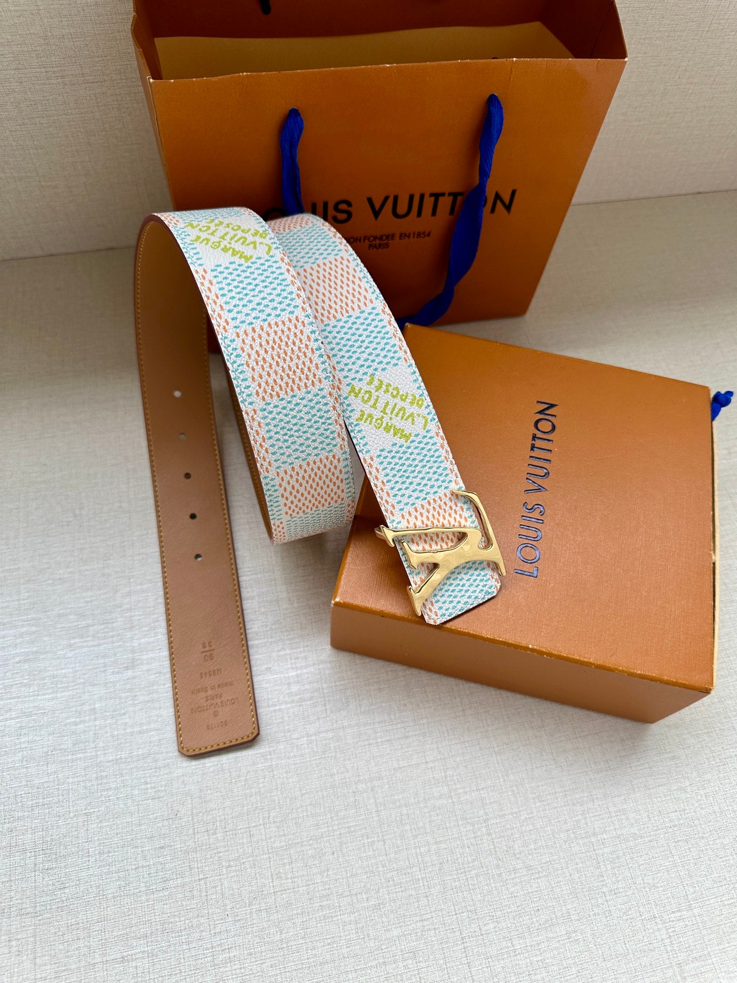Louis Vuitton belt with light blue and white pattern, metal buckle, tan leather end tab.