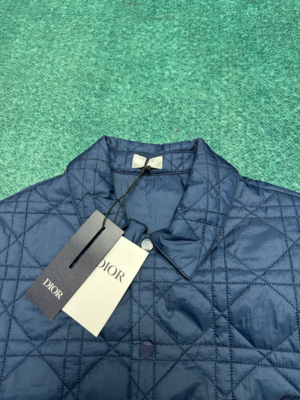 Navy quilted jacket with diamond pattern, logo patch, and attached tags