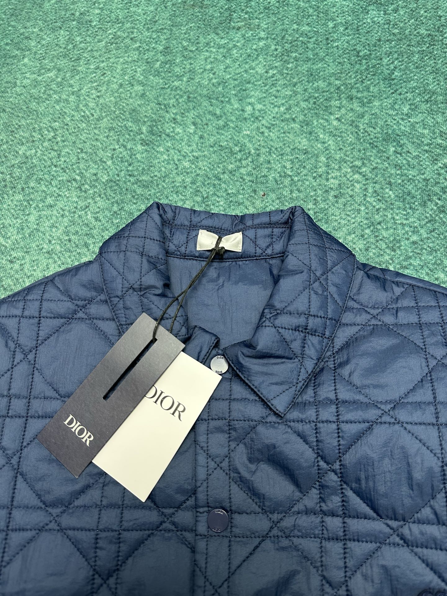 Navy quilted jacket with diamond pattern, logo patch, and attached tags