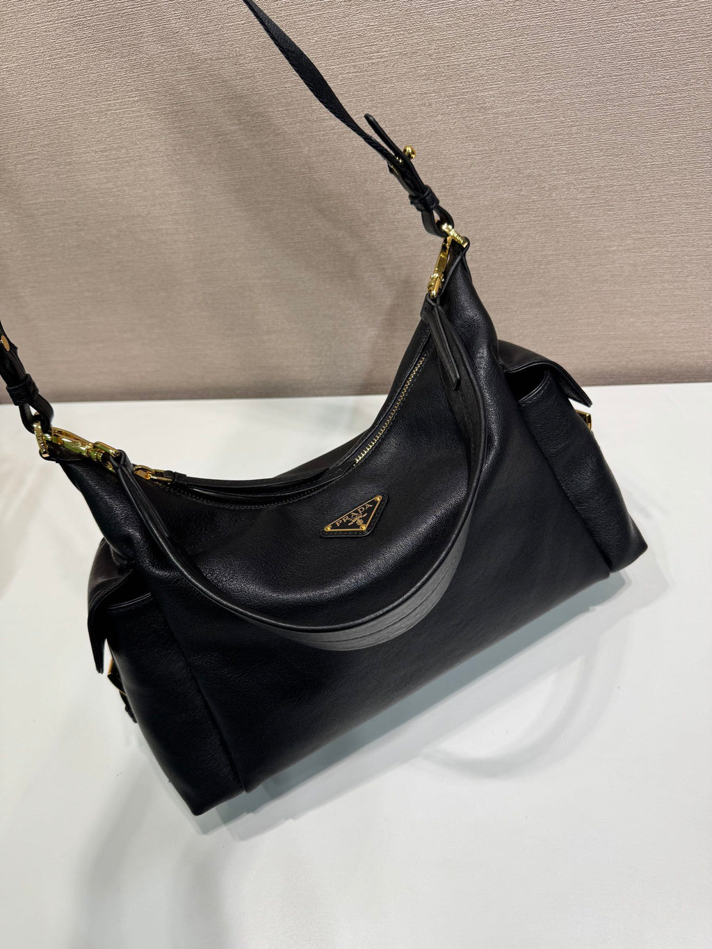 Black Prada shoulder bag angled view with gold-tone rings and slouchy silhouette.