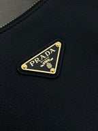 Prada black leather bag with gold logo plaque on textured surface.