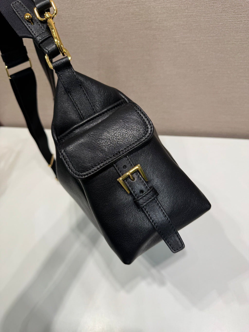 Prada black leather crossbody pouch with gold buckle and small flap pocket.