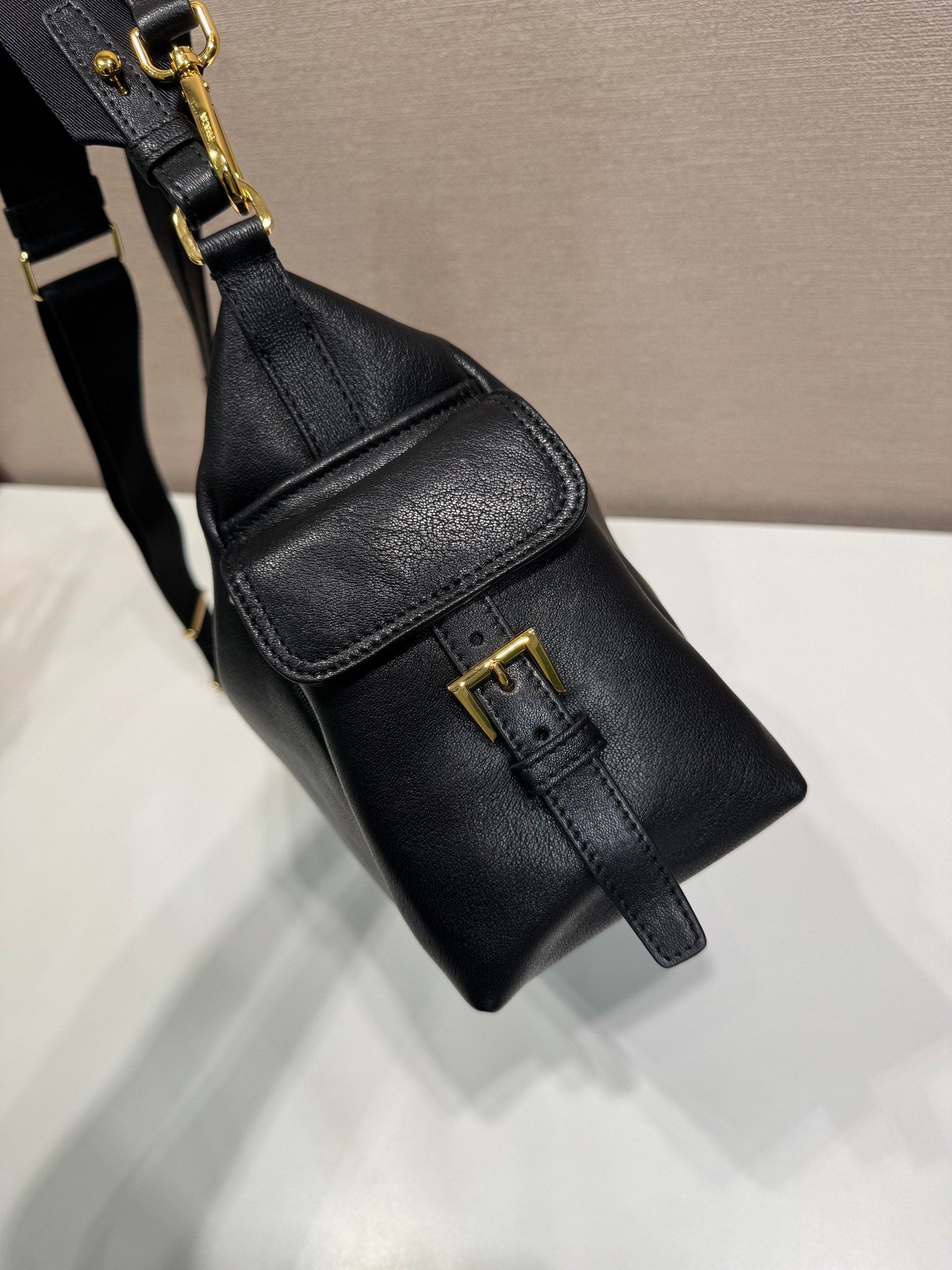 Prada black leather crossbody pouch with gold buckle and small flap pocket.