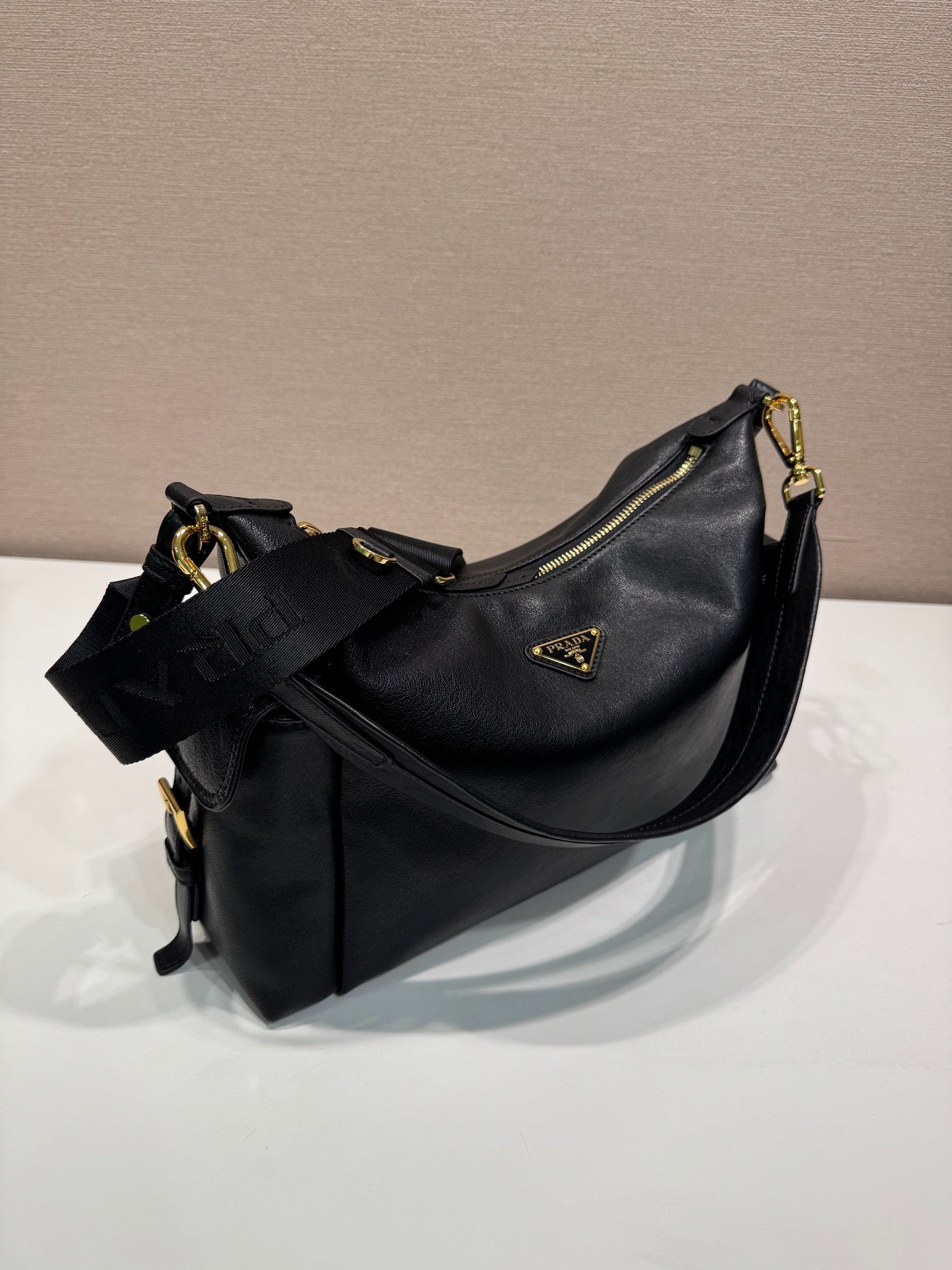 Black Prada shoulder bag with curved hobo shape, gold hardware, and front zip detail.
