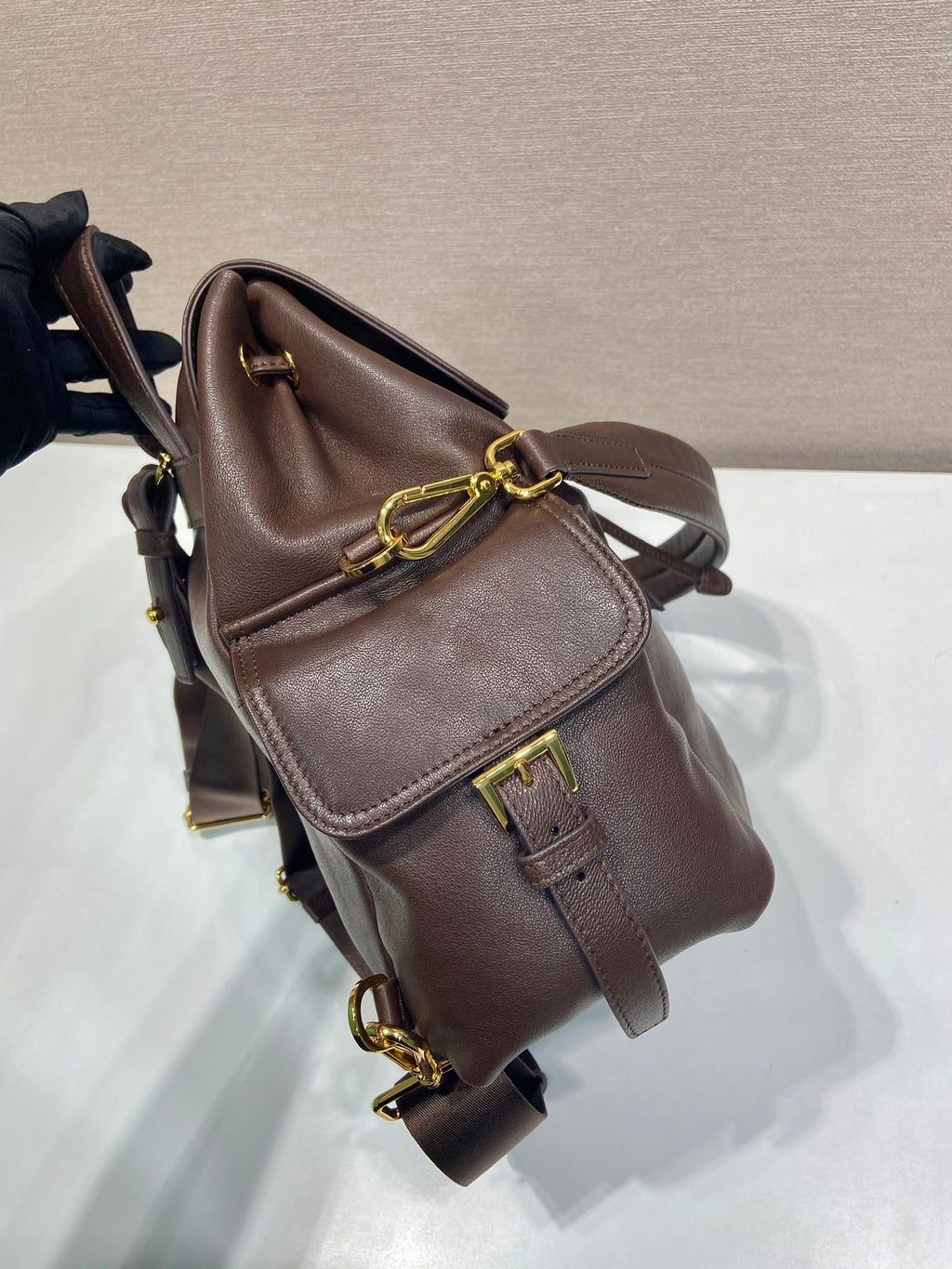 Brown leather mini backpack with top handle, flap closure, and gold chain accents