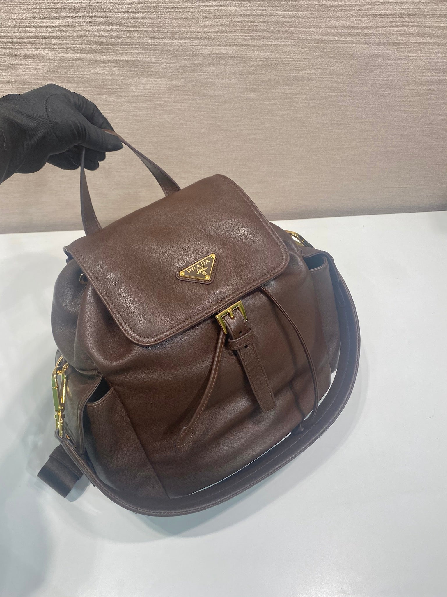 Brown leather mini backpack with flap and strap, shown from upper side angle