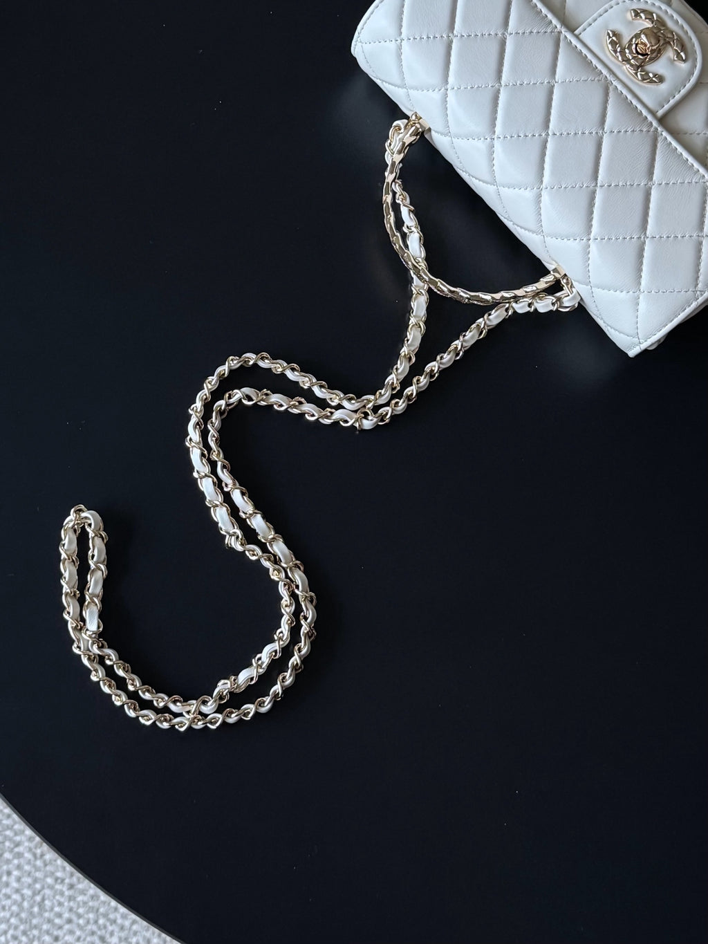 Chanel white quilted flap bag with chain strap on black surface