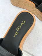 Black slide sandal close-up with gold script logo on footbed and cork edge