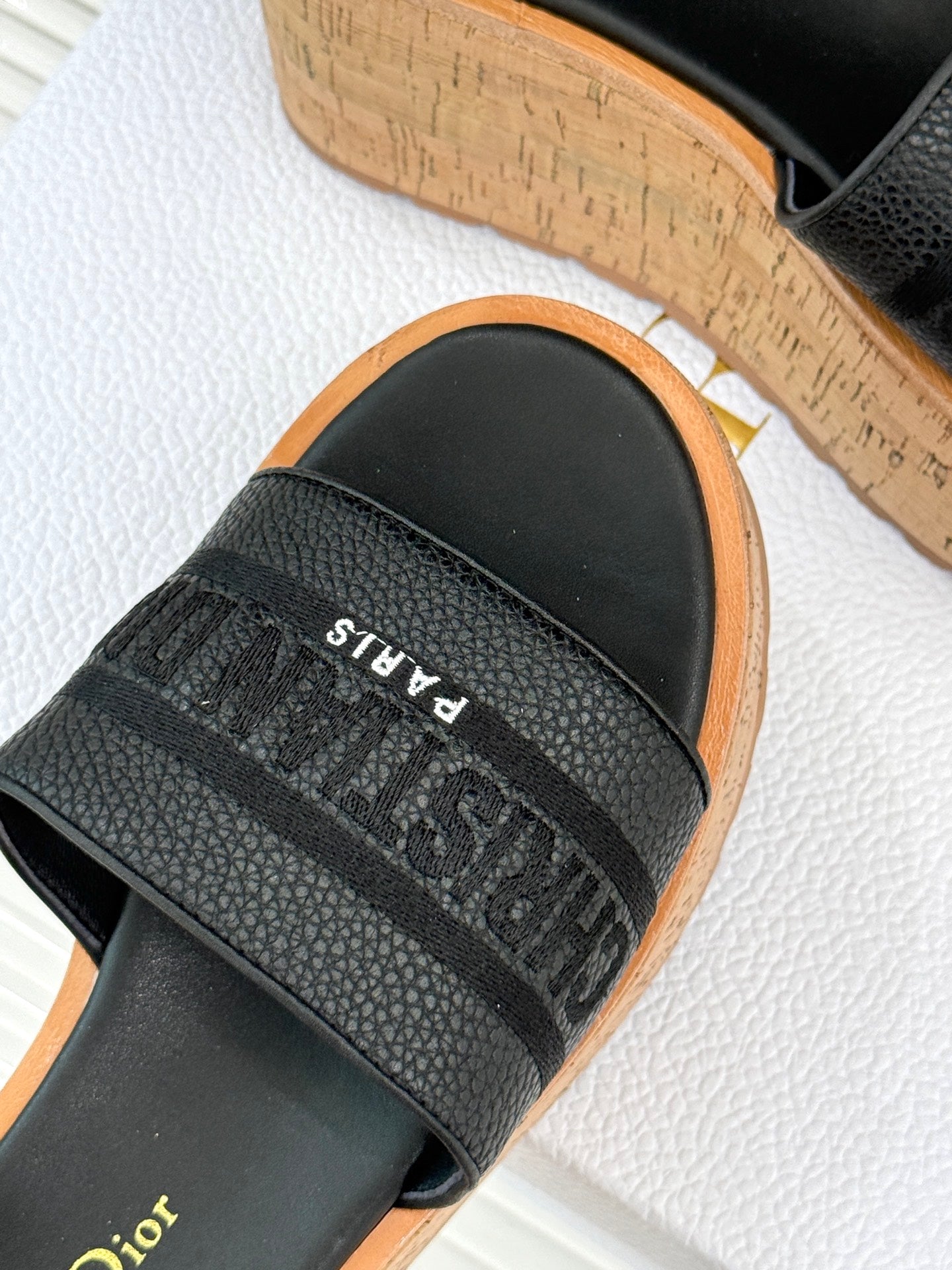 Black platform slide sandal close-up with textured strap and white 'PARIS' print