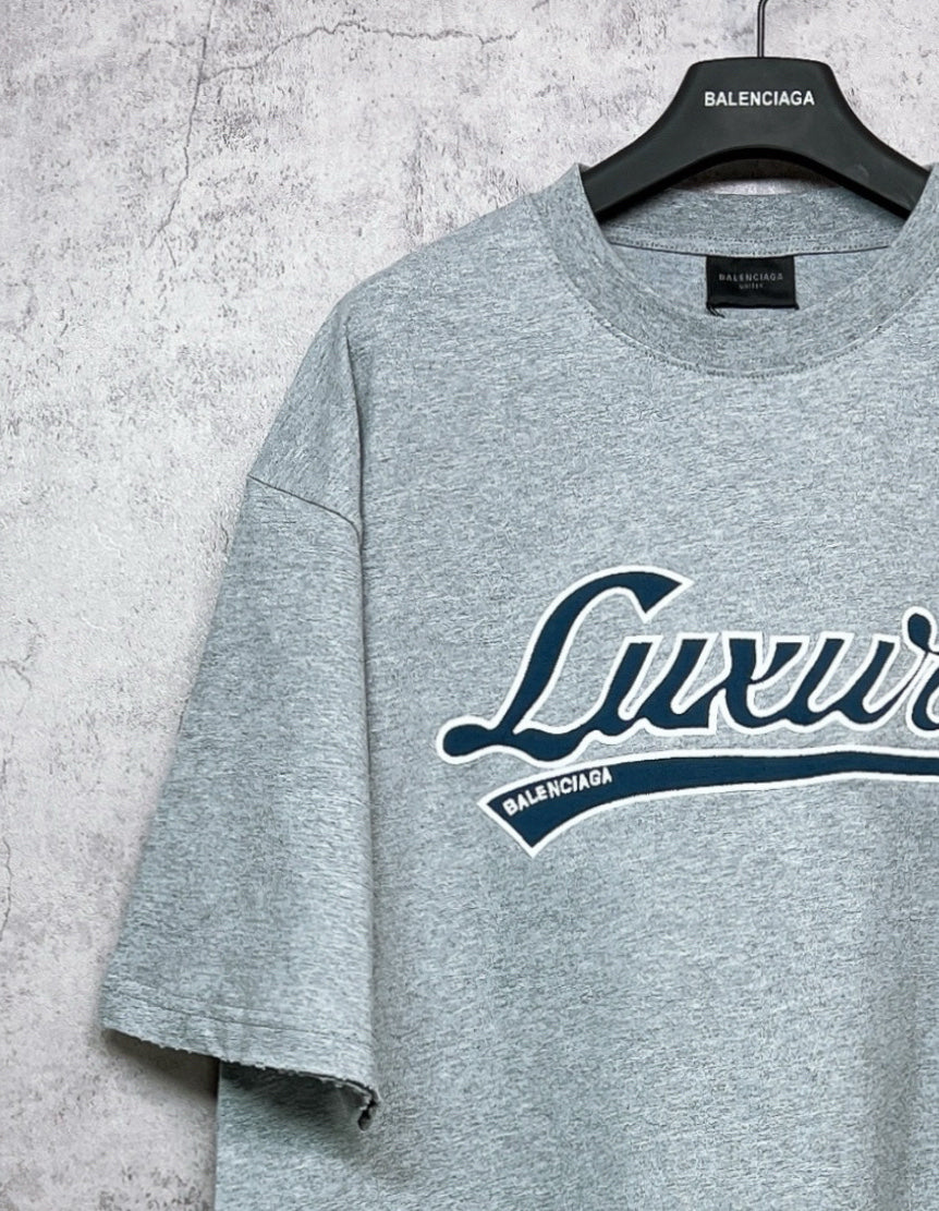 Balenciaga heather gray T-shirt angled view, “Luxury” logo partially visible