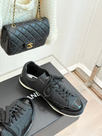 Dark lace-up sneakers with Chanel CC logo on side, on gray shoebox