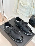 Two dark lace-up sneakers with Chanel CC emblem and white sole trim
