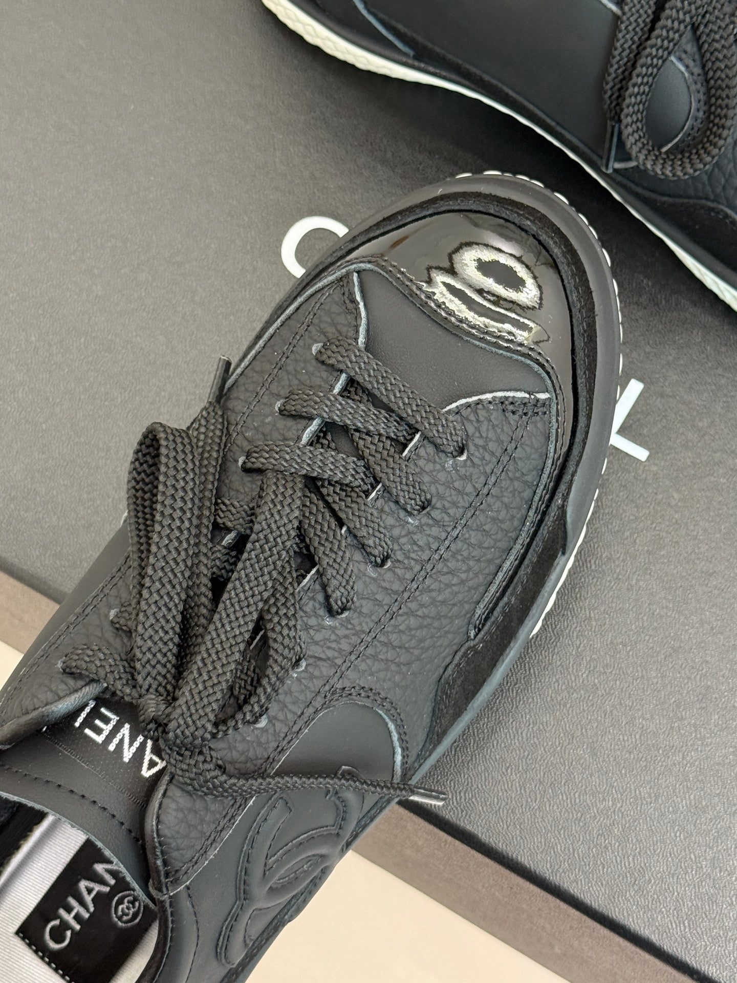 Close-up of dark lace-up sneaker toe with Chanel CC patch and laces