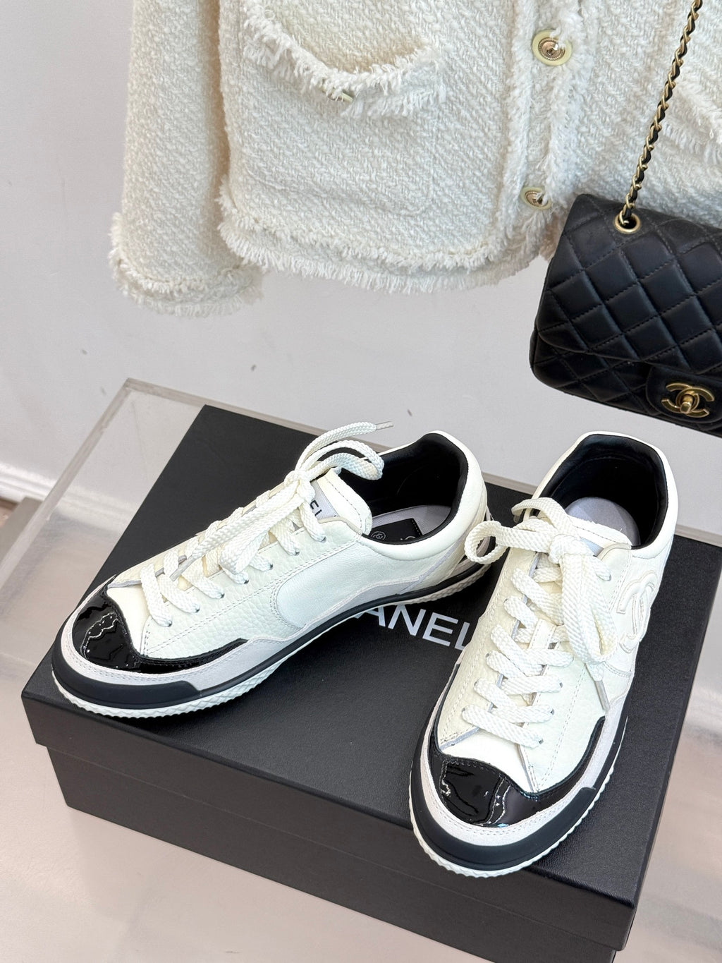 White low-top sneakers with CHANEL side logo, black trim, and white laces