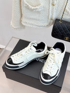 White low-top sneakers with CHANEL side logo, black trim, and white laces