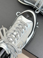 Close-up of metallic silver sneaker toe area with lace-up bow and black-trim sole edge