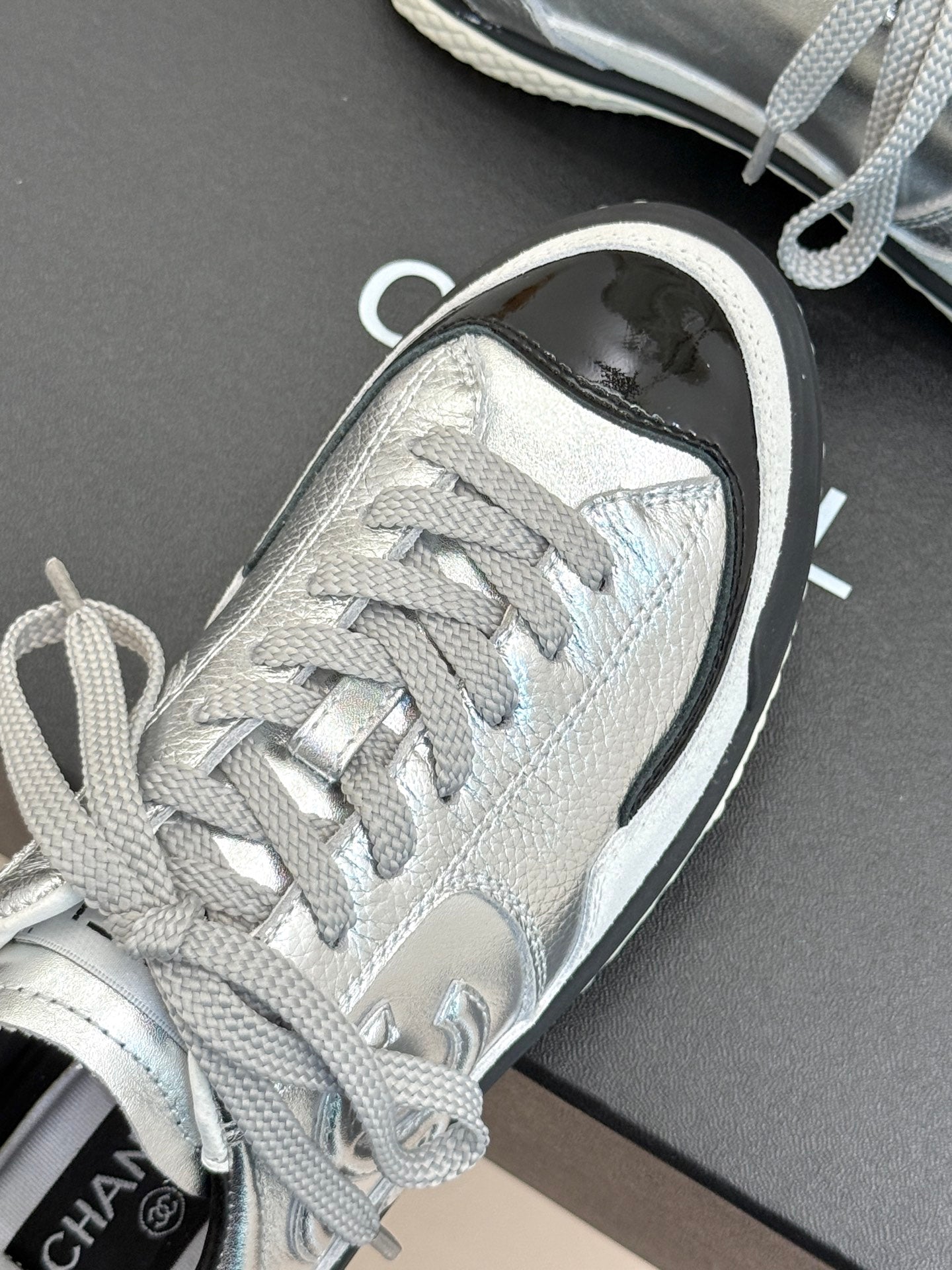 Close-up of metallic silver sneaker toe area with lace-up bow and black-trim sole edge