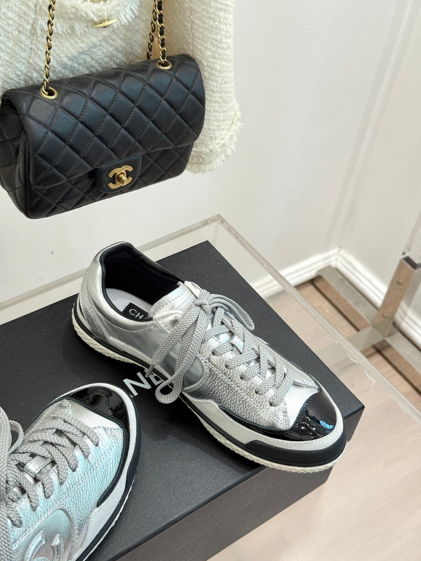 Metallic silver sneakers with black-trim soles and lace-up uppers, placed on a box