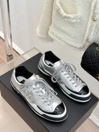 Metallic silver Chanel sneakers pair on a black display box, lace-up style with black trim