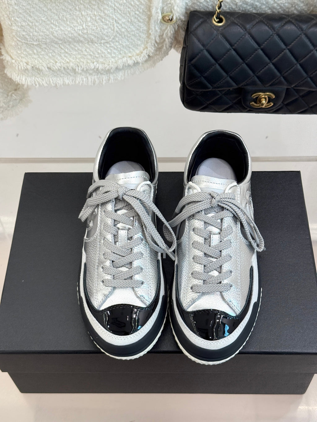 Silver lace-up low-top sneakers with black side panels and white laces, pair on a box