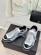Silver lace-up low-top sneakers with black accents, shown as a paired set on a box