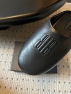 Balenciaga slide sandal close-up, embossed logo on dark leather upper